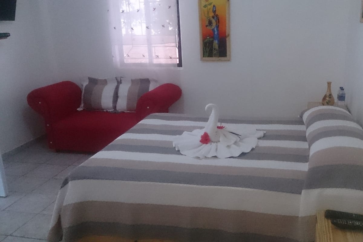 Quarto com cama, sofá vermelho, quadro na parede e janela com cortinas.