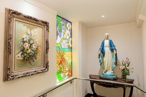 Eine Statue einer religiösen Figur auf einem Sockel, ein gerahmtes Blumenbild und ein Buntglasfenster.