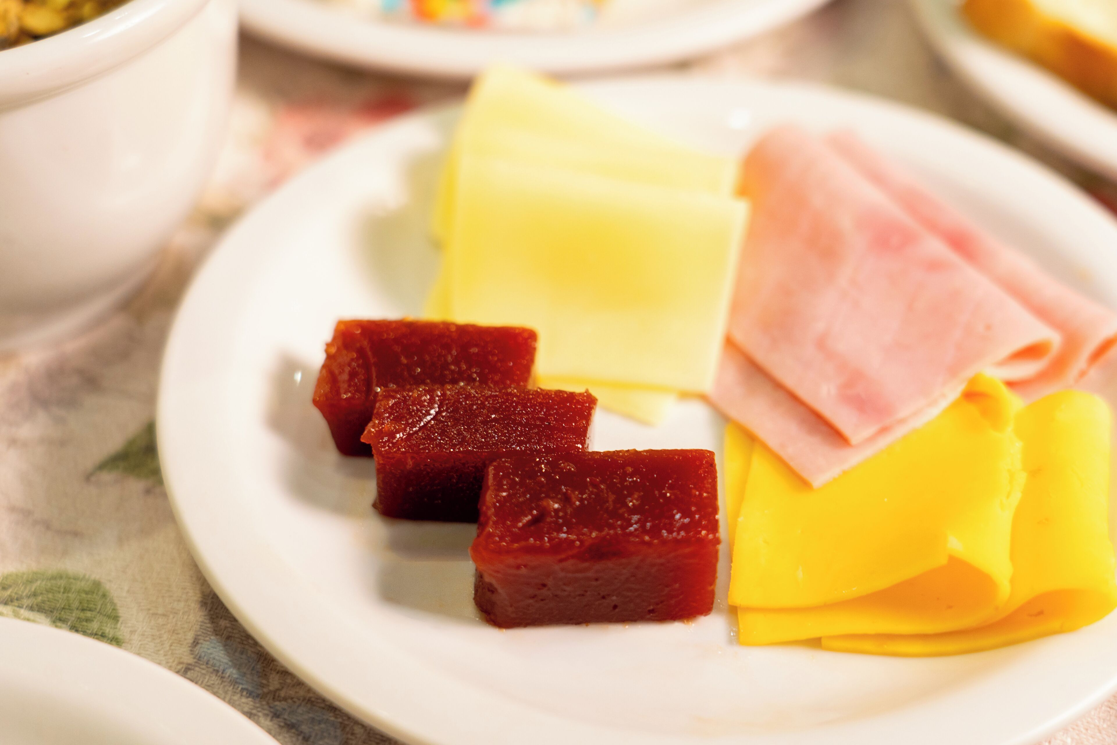 Un plato con rebanadas de queso amarillo, carne roja y un aderezo amarillo.