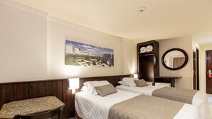 Habitación de hotel con dos camas, un escritorio, una silla, un cuadro grande, un espejo y un armario.