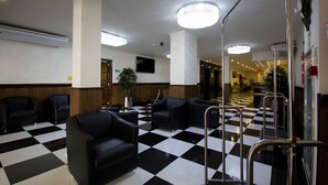 Un hall con suelo de cuadros, asientos de cuero negro, un espejo grande y una lámpara en el techo.