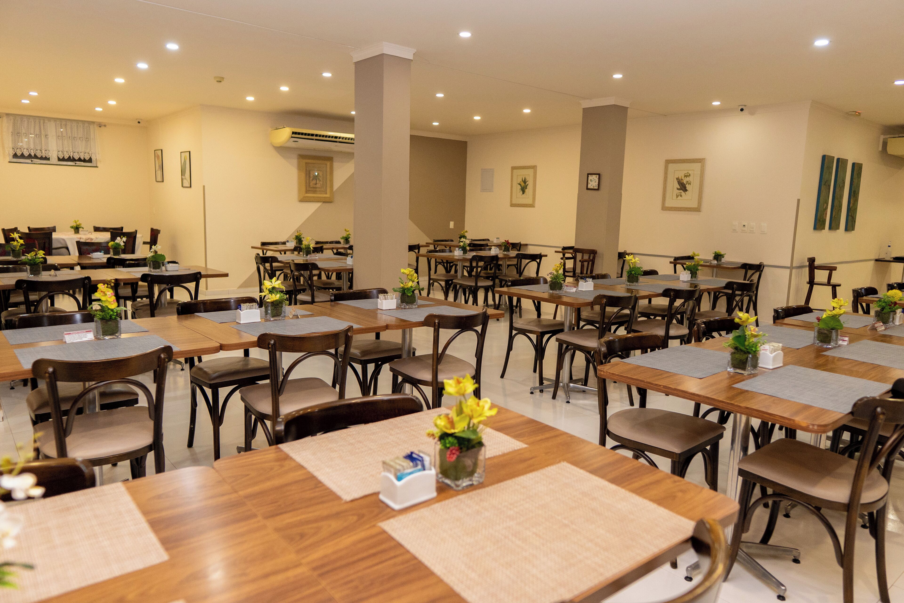 Uma sala de jantar de hotel com várias mesas e cadeiras, dispostas num espaço amplo.