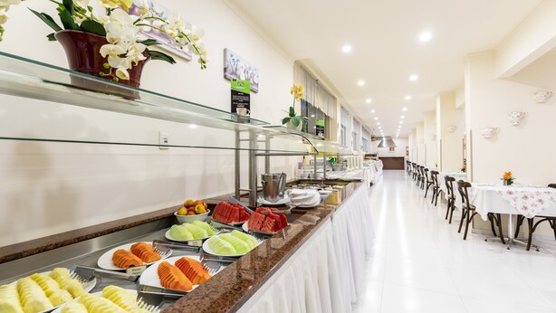Zona de bufé con diversas opciones de comida, incluyendo frutas y postres, y un área de estar con mesas y sillas.