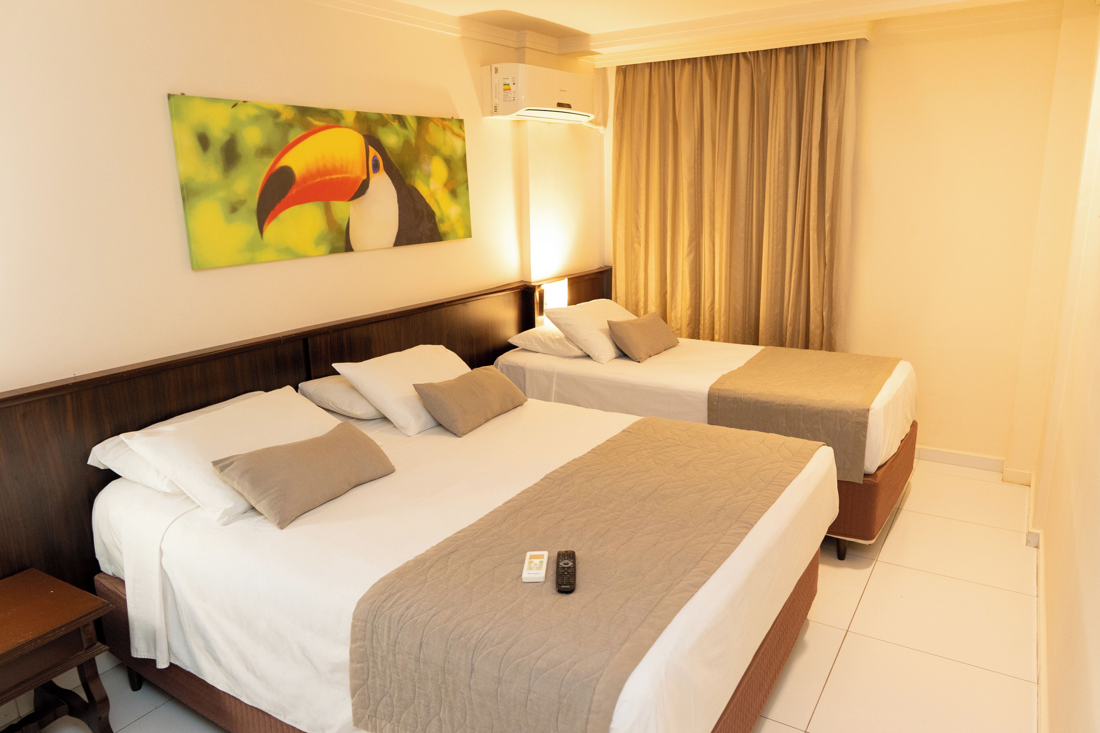 A hotel room with two beds, a nightstand, a remote control, and a painting on the wall.