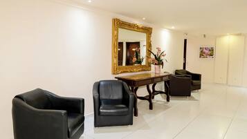 A reception area with a large mirror, two leather chairs, a wooden table, and a vase with flowers.
