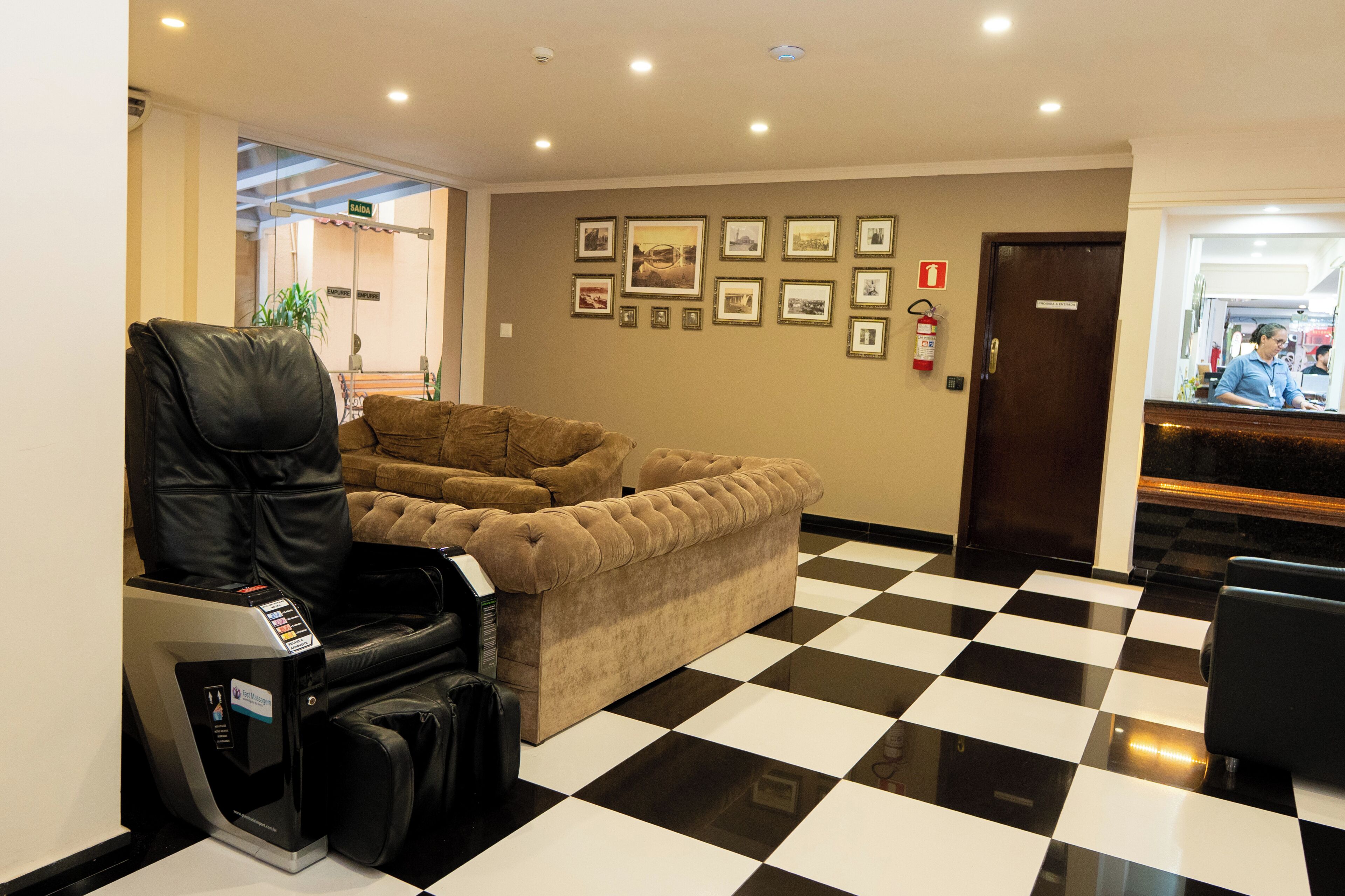 Un hall d’hôtel avec un fauteuil de massage, un sol à carreaux, des tableaux encadrés accrochés au mur et un comptoir de réception.