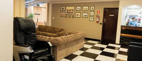 Un hall d’hôtel avec un fauteuil de massage, un sol à carreaux, des tableaux encadrés accrochés au mur et un comptoir de réception.