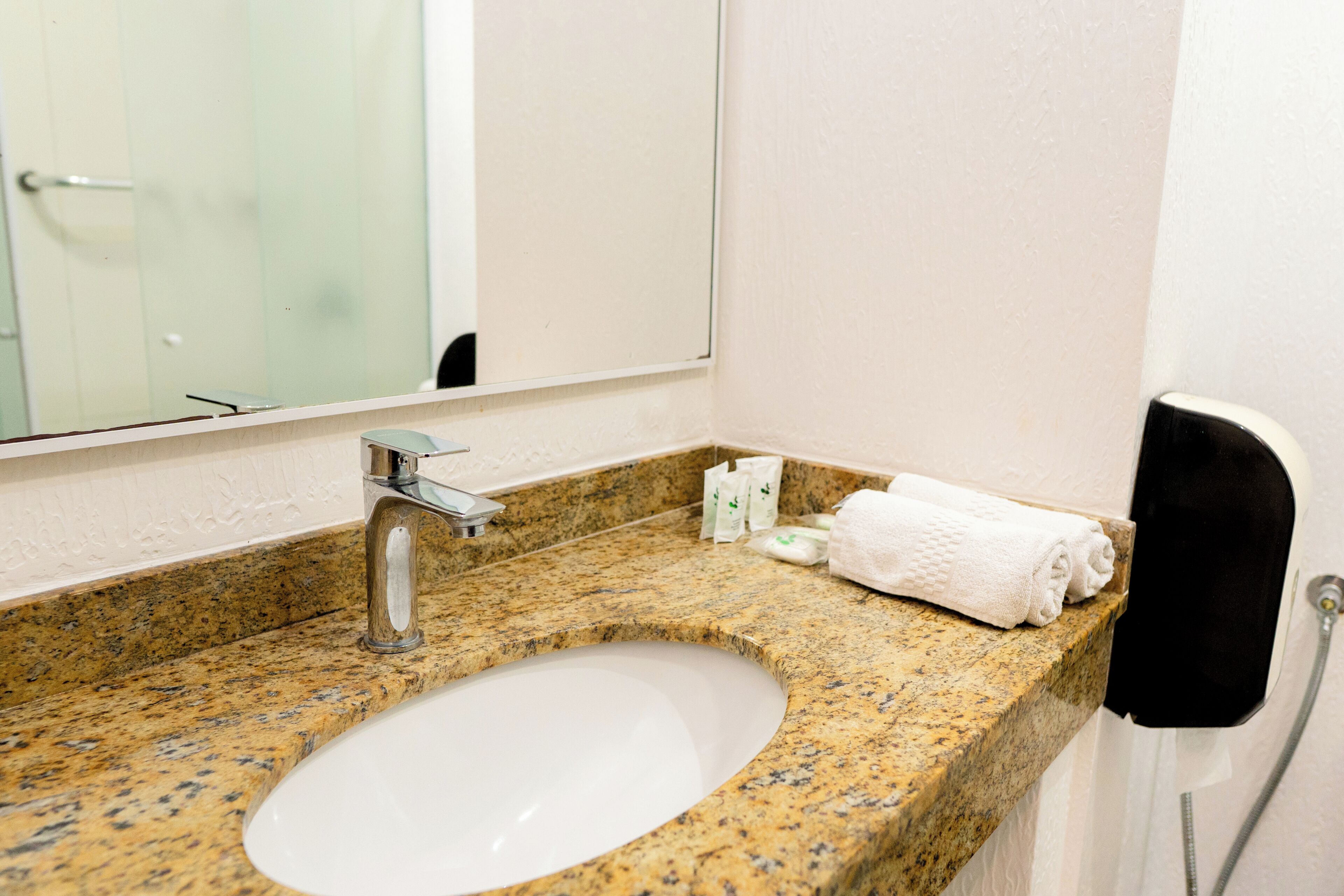 Une salle de bain avec un comptoir en granit, un lavabo blanc, un miroir et un porte-serviettes.