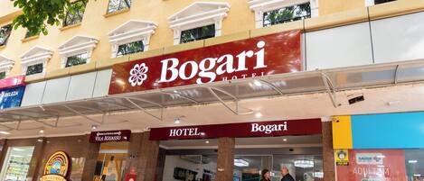 A hotel named Bogari with a prominent red sign, a visible entrance, and a surrounding area with potted plants.