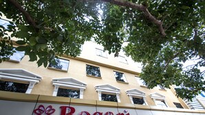 Exterior del hotel Bogari, con un cartel llamativo, amplias ventanas y un árbol en primer plano.