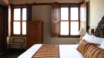 Un dormitorio con cama, mesita de noche, lámpara, armario y dos ventanas con cortinas.