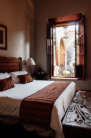 A hotel room with a large bed, a nightstand with a lamp, and a window with an open shutter.