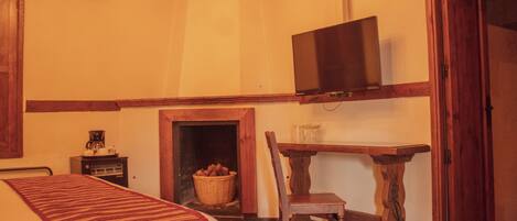 A cozy room with a bed, a television mounted on the wall, a wooden table, a chair, and a fireplace.