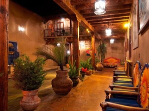 A cozy, dimly lit corridor with wooden beams, potted plants, and a bench with colorful cushions.