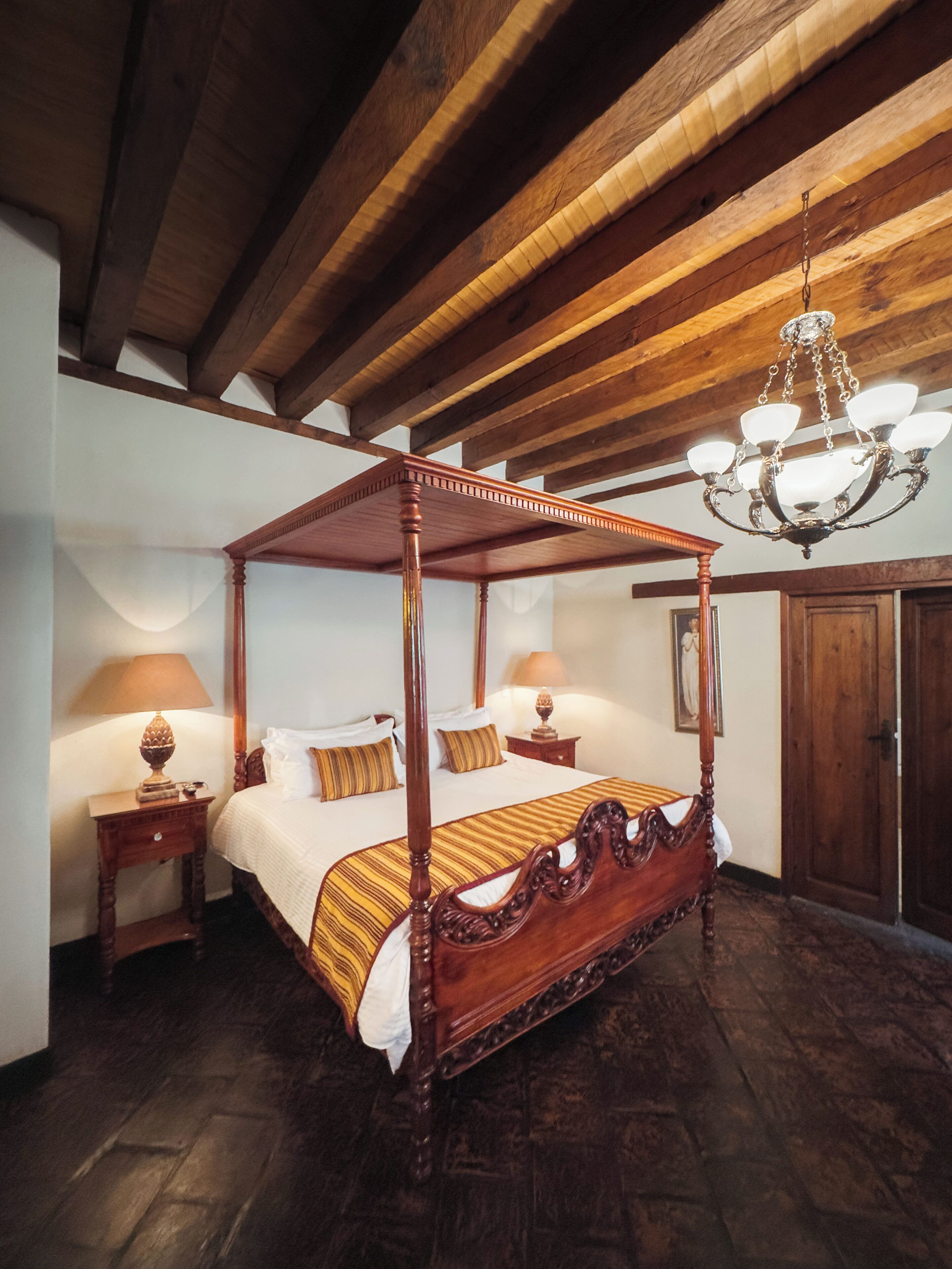 A four-poster bed with a canopy, wooden flooring, and a chandelier.