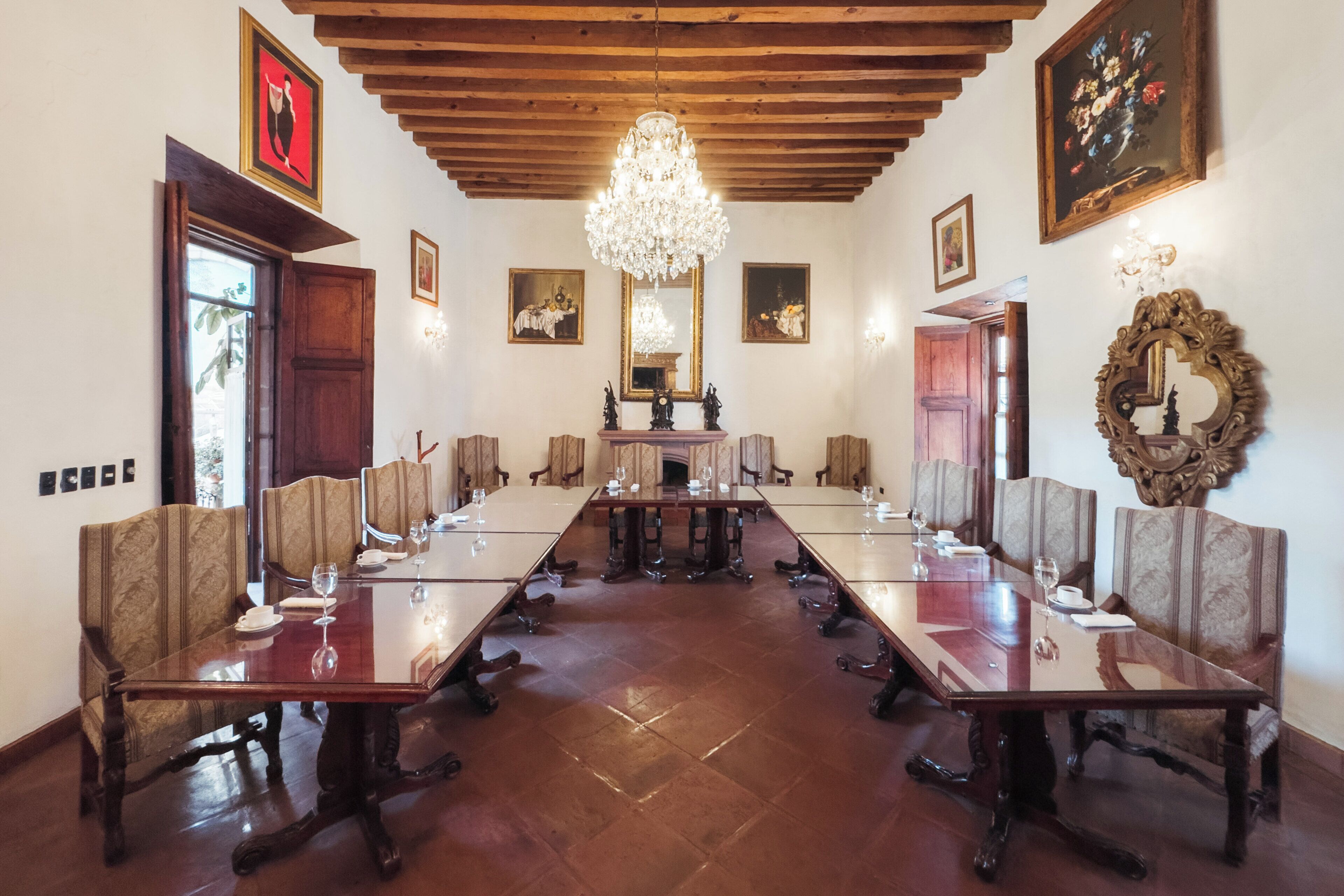 A conference room with a long table, chairs, a chandelier, and framed artwork on the walls.