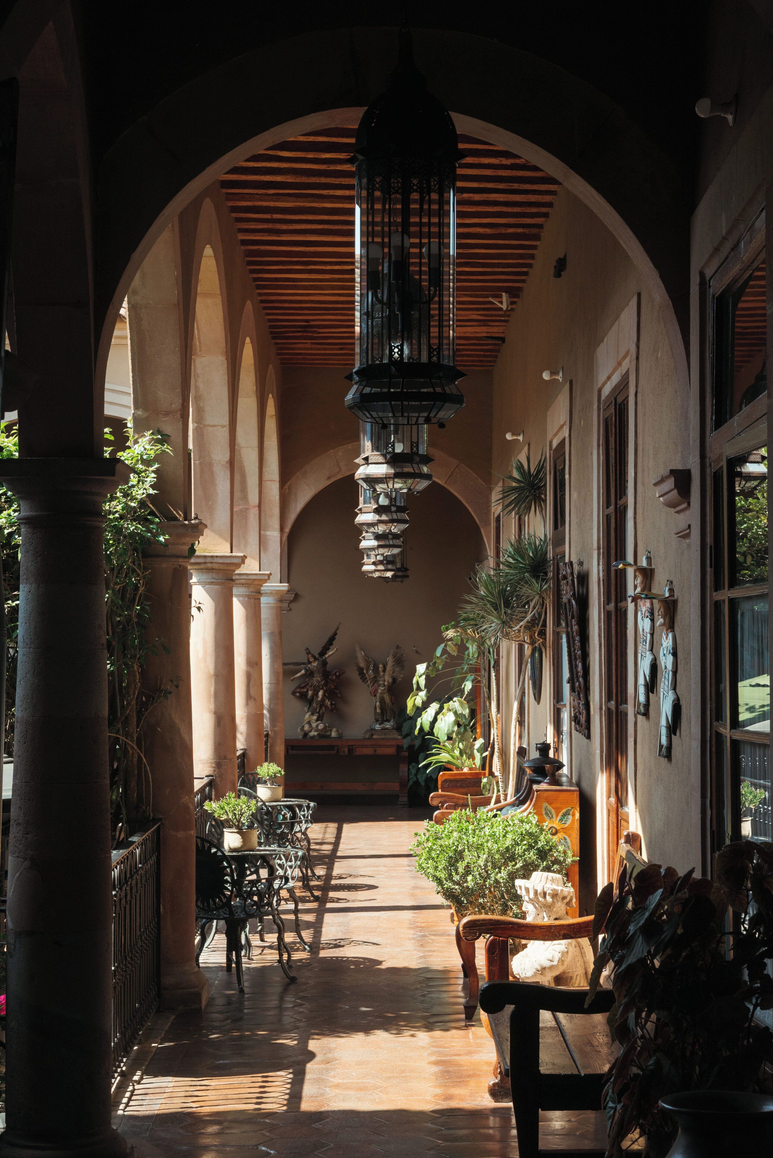 Un corredor abovedado con columnas, techo de madera y plantas en macetas.
