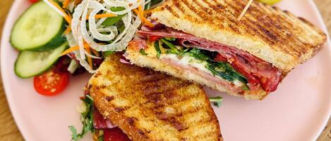 Un panino tagliato a metà su un piatto rosa, accompagnato da un'insalata e fette di cetriolo.