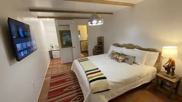 A bedroom with a bed, a TV mounted on the wall, a bedside lamp, and a patterned rug.
