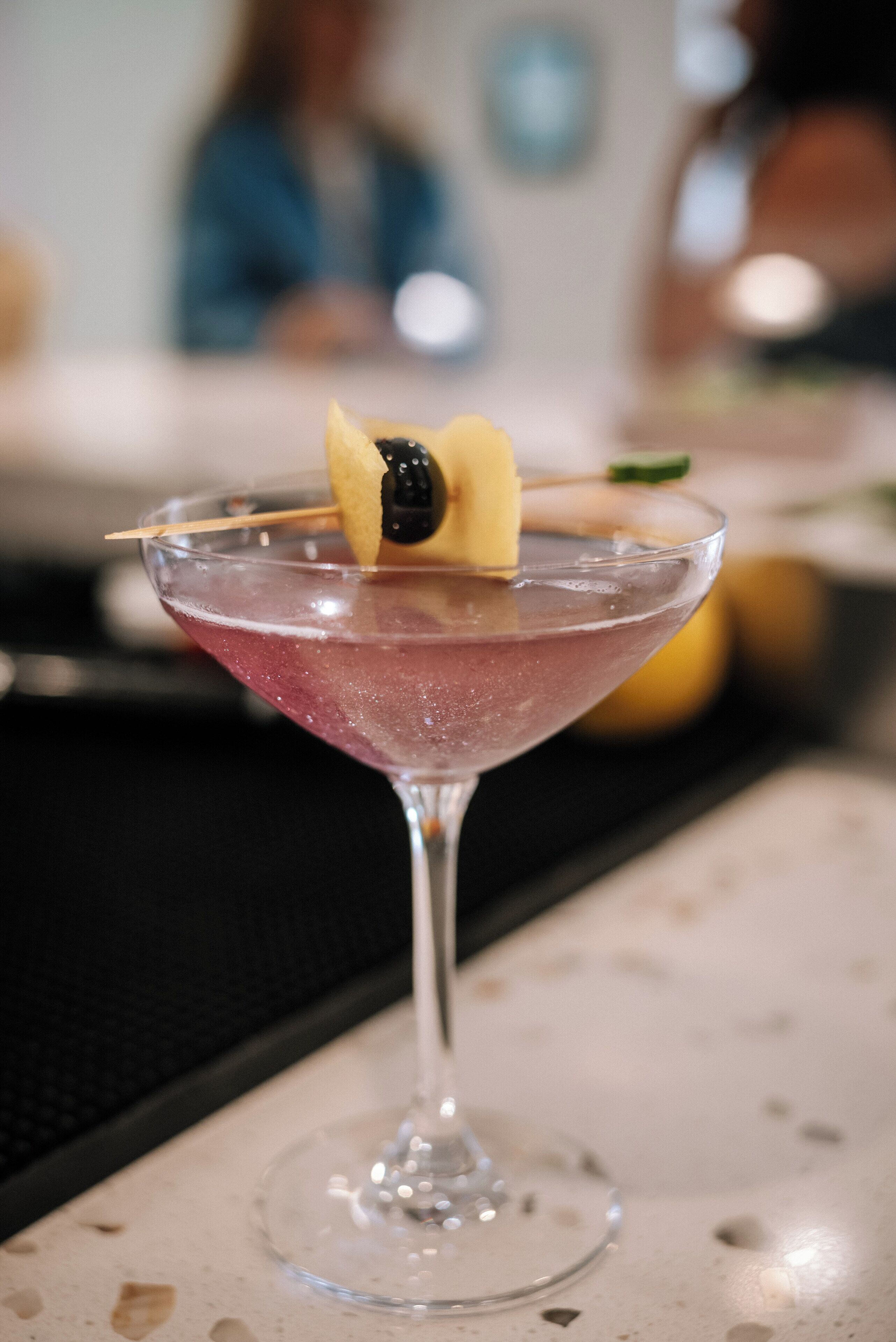 Cocktail-drinkki tarjoiltuna martiniglasissa, jossa on koriste, ja se on asetettu pöydälle.