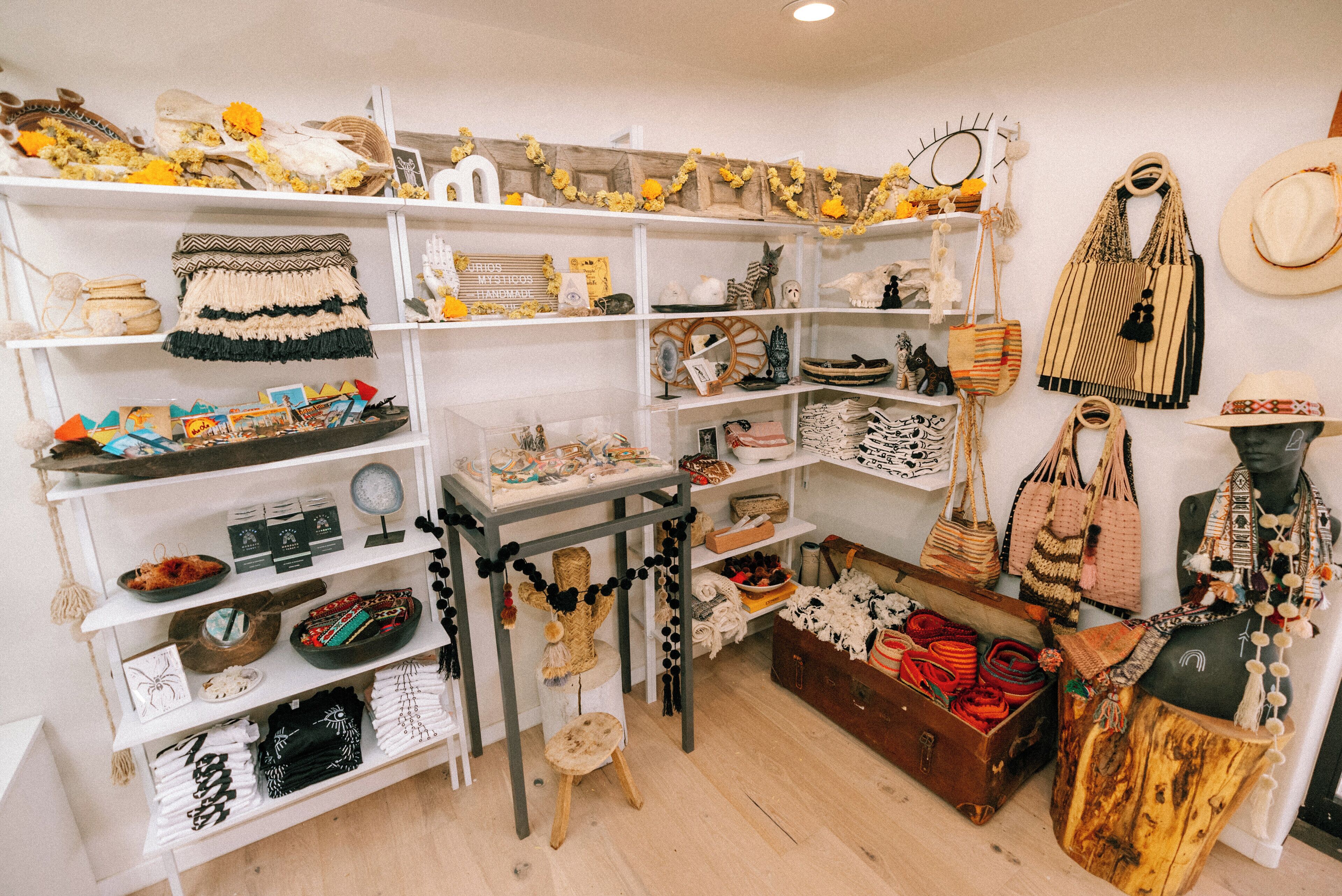 Uma loja boutique com prateleiras cheias de bolsas, acessórios e um manequim vestido com traje típico.