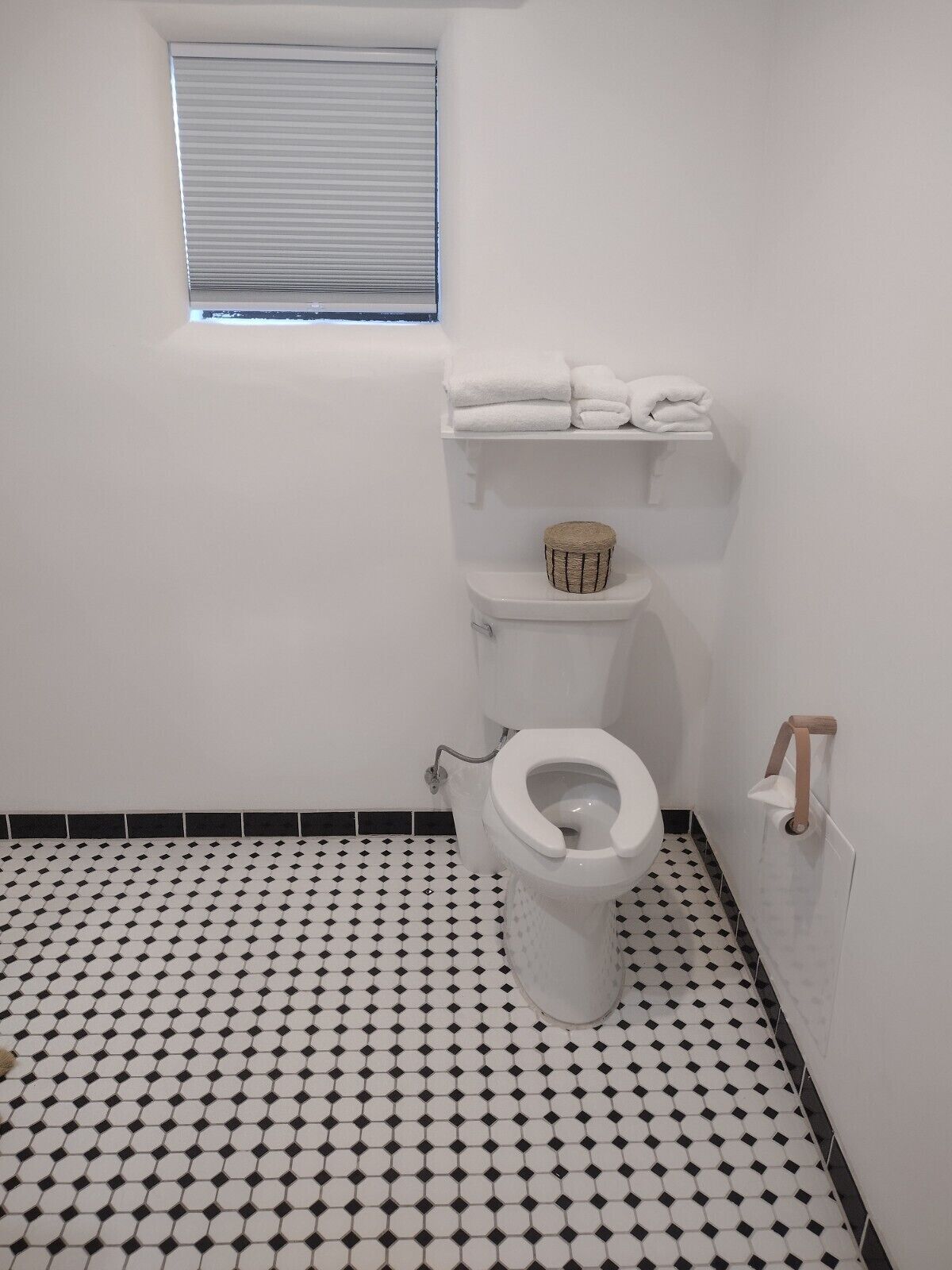 A bathroom with a toilet, a shelf with towels, a small window, and a patterned floor.