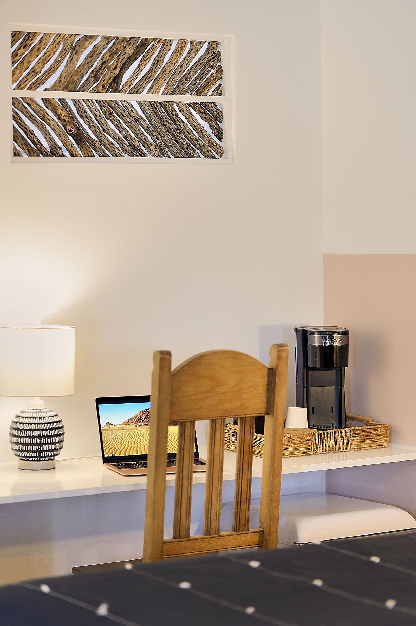 A bedroom with a wooden headboard, a laptop on a bedside table, a coffee maker, a lamp, and a wall art piece.