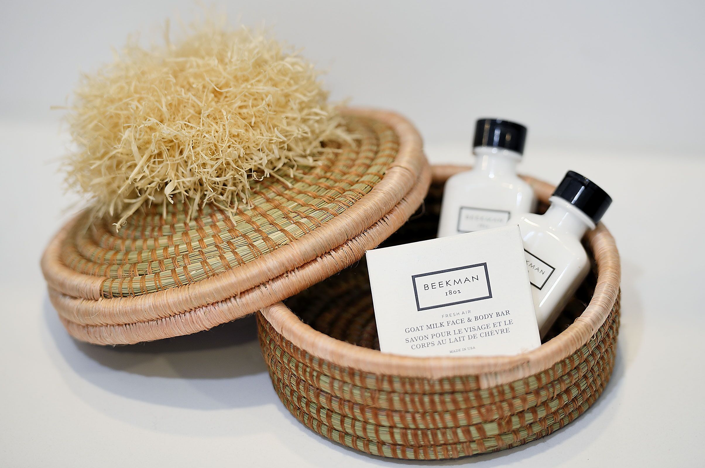 A wicker basket containing a bottle of goat milk soap, a bottle of body lotion, and a sachet of exfoliating beads.