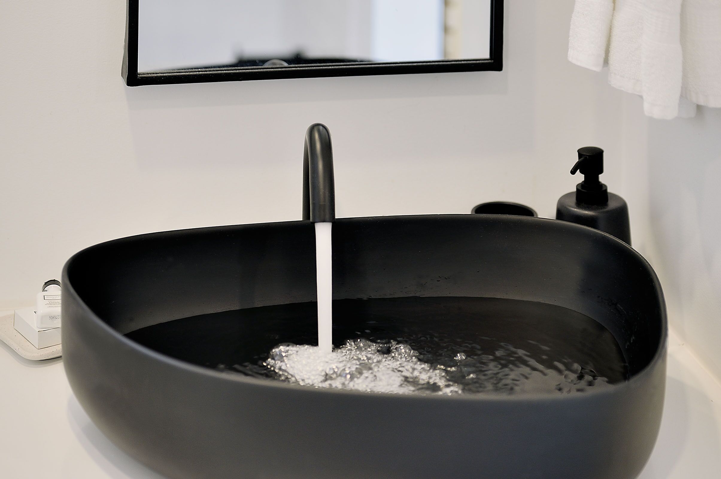 A black basin with a faucet, a soap dispenser, and a power outlet on a white countertop.