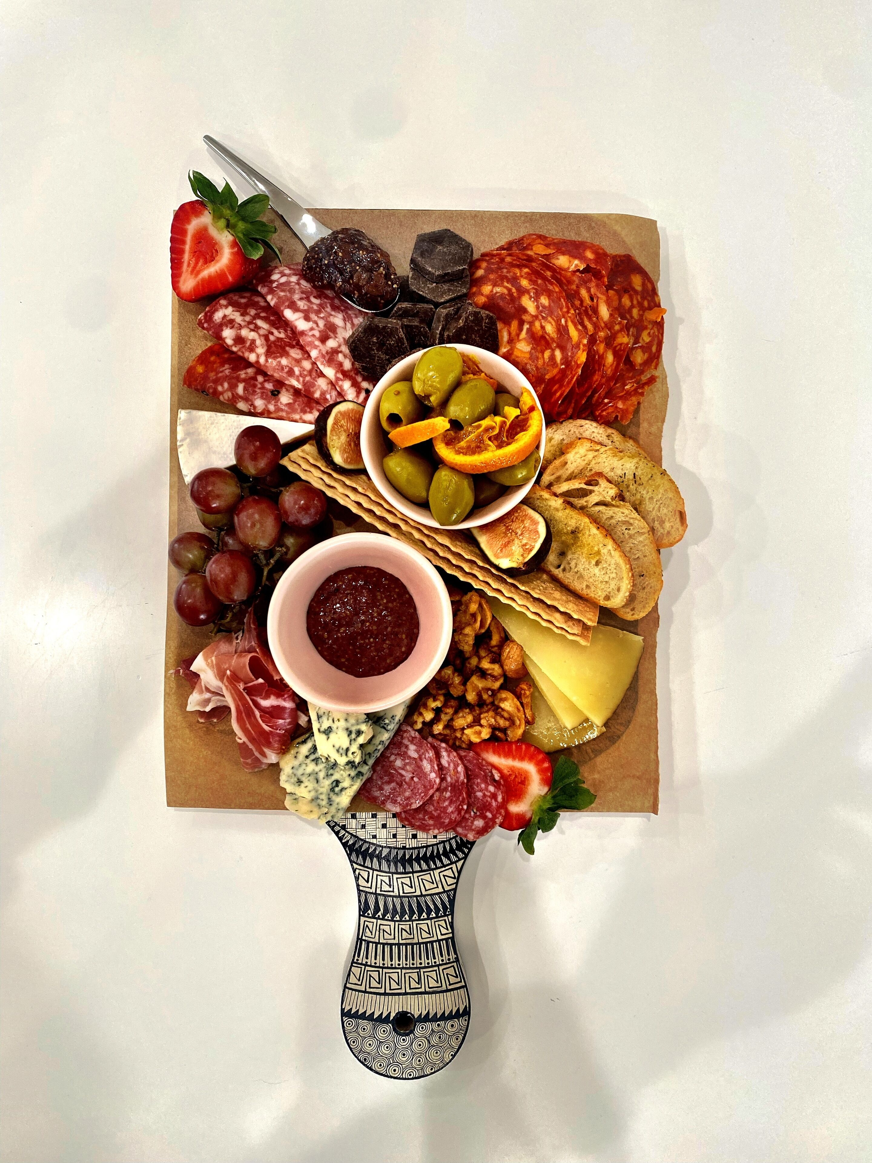Une planche de charcuterie comprenant différentes sortes de viandes, de fromages, de fruits et de noix.