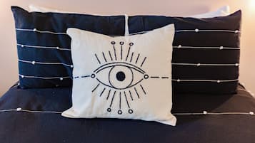 Ein Bett mit einem weißen Kopfkissen mit einem Augenmotiv, umrahmt von zwei dunklen Kissen.
