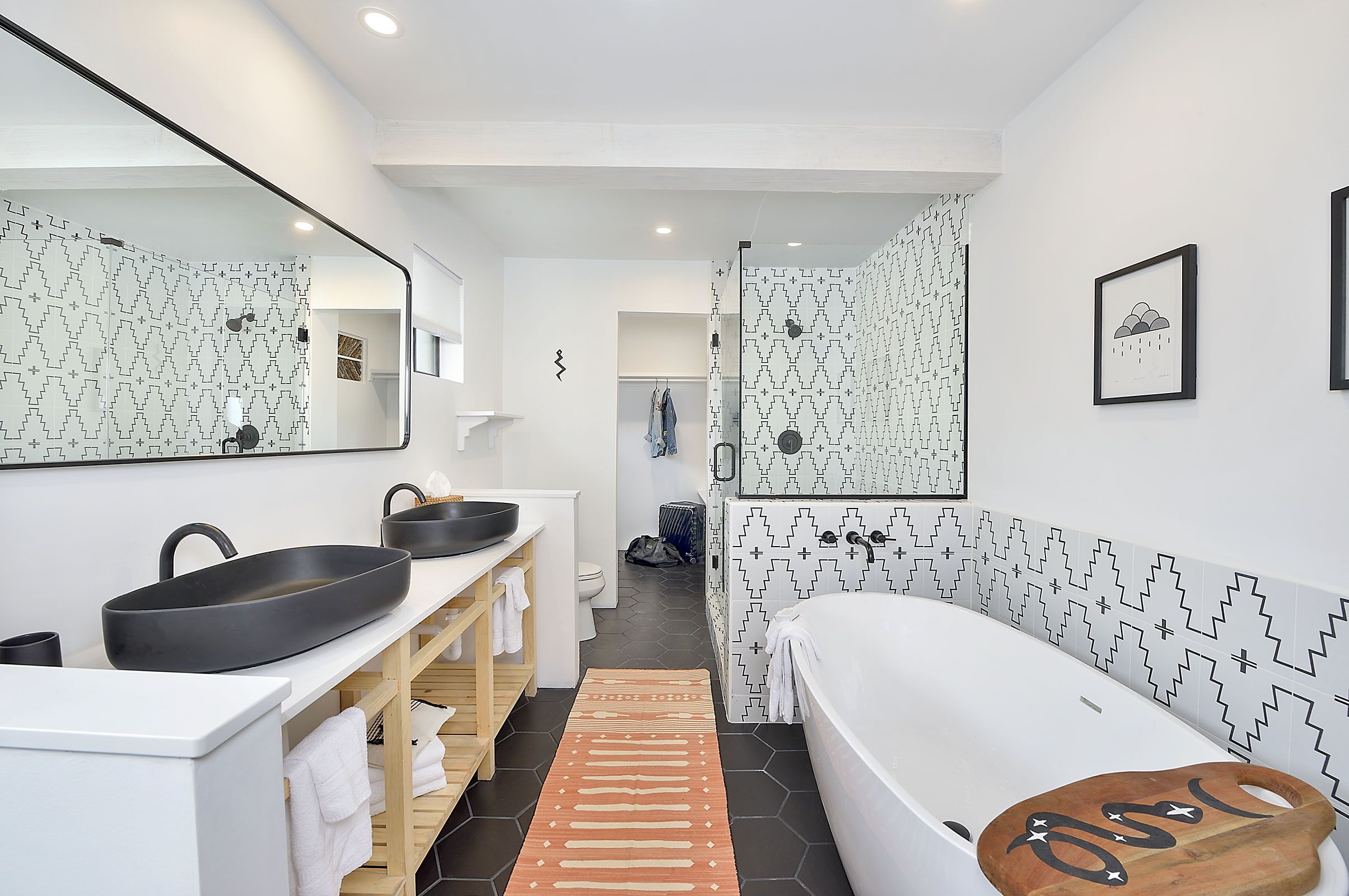 Um banheiro moderno com um espelho grande, pia preta, banheira branca e azulejos estampados.