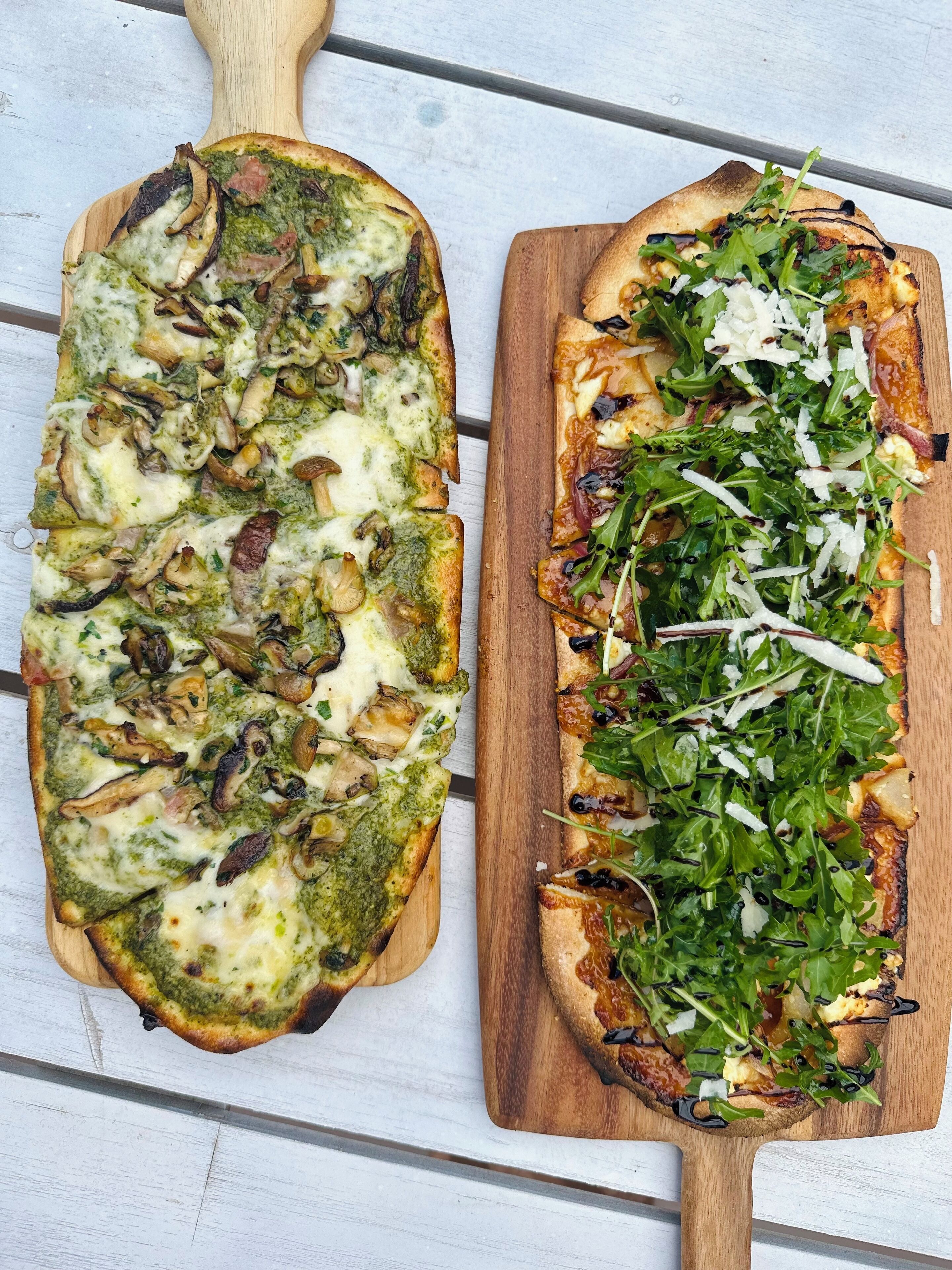 Two pizzas on wooden boards.