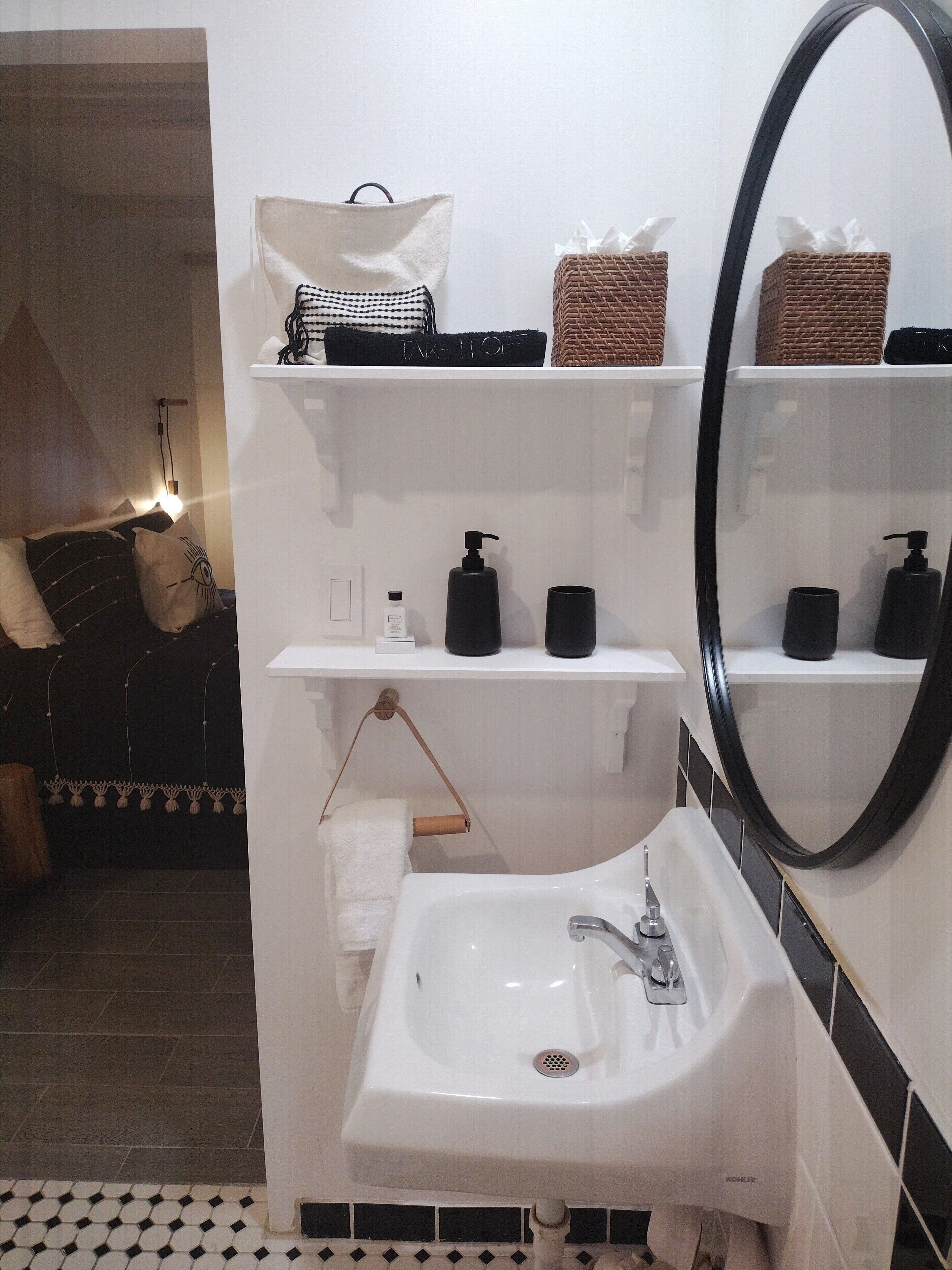 Ein Badezimmer mit einem weißen Waschbecken, schwarzen Seifenspendern, einem Handtuchhalter und einem Spiegel.