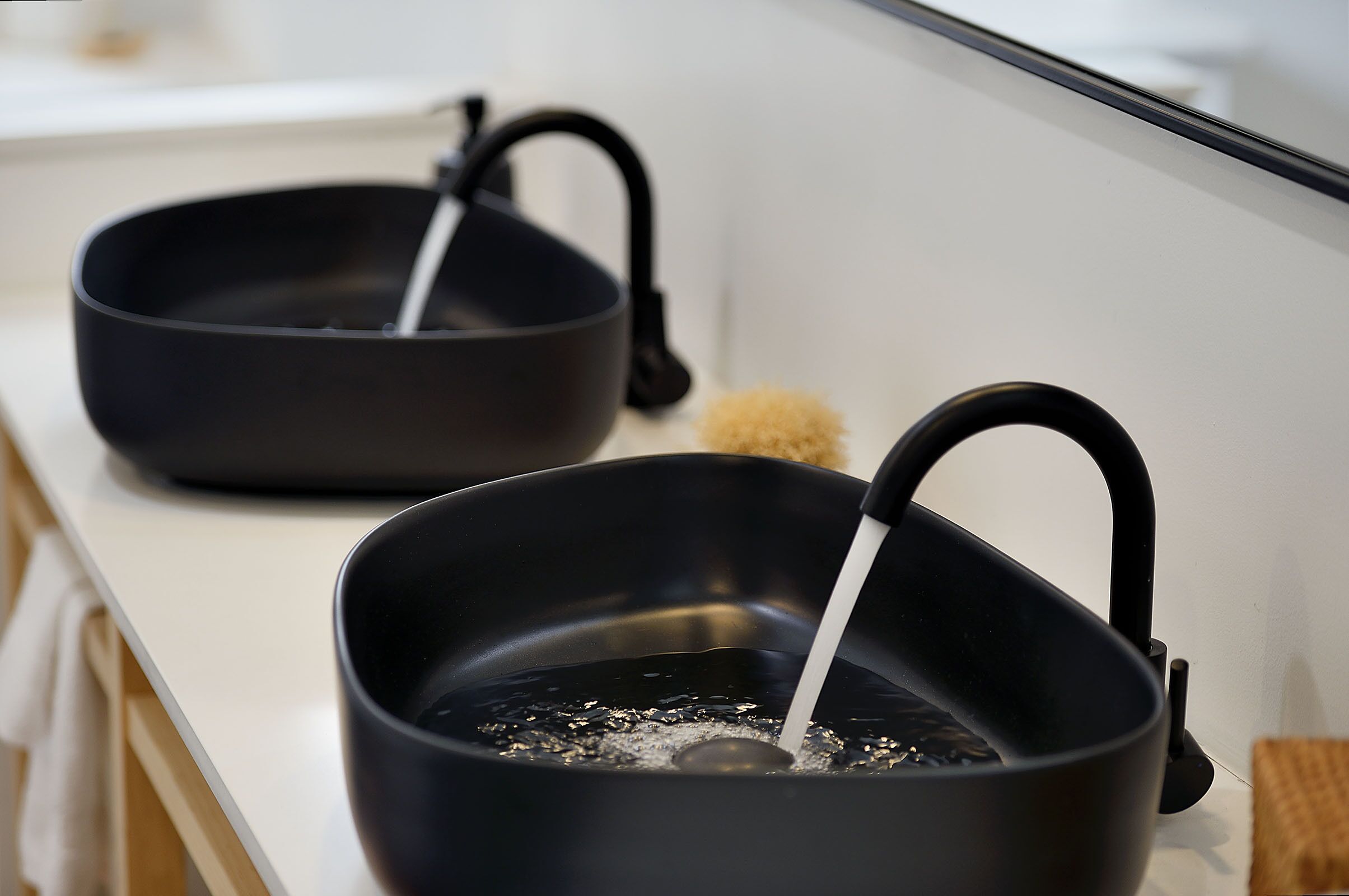 Two black frying pans on a white countertop with a wooden cutting board and a white cloth.