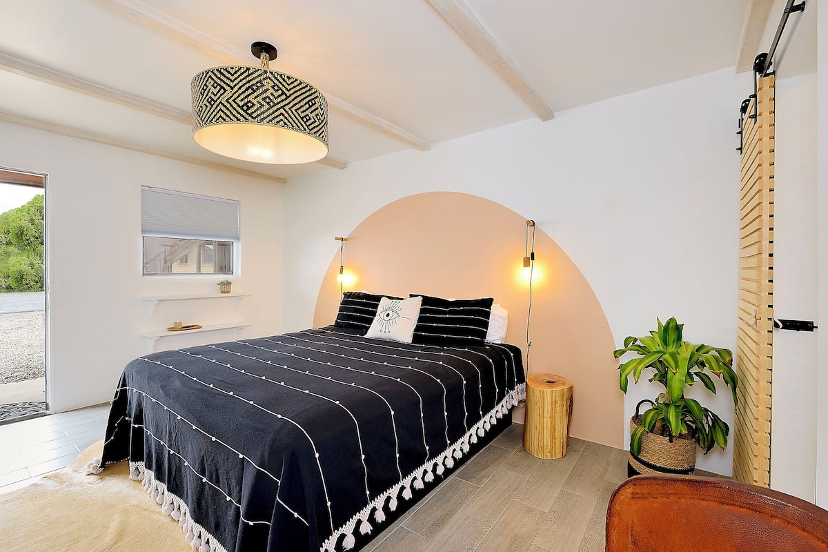 Une chambre avec une couvre-lit à rayures noires et blanches, un luminaire suspendu, une table de chevet en bois et une plante en pot.
