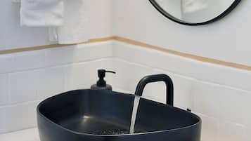 Un baño con un lavabo negro, un espejo y un perchero con toallas blancas.