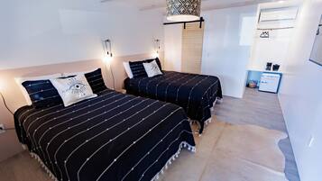 Ein Schlafzimmer mit zwei Betten, einer Hängeleuchte, einer kleinen Küchenzeile und einem Kuhfellteppich.