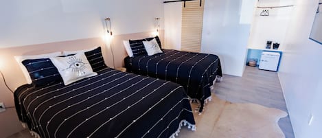 Un dormitorio con dos camas, una lámpara colgante, una pequeña kitchenette y un tapete de cuero de vaca.