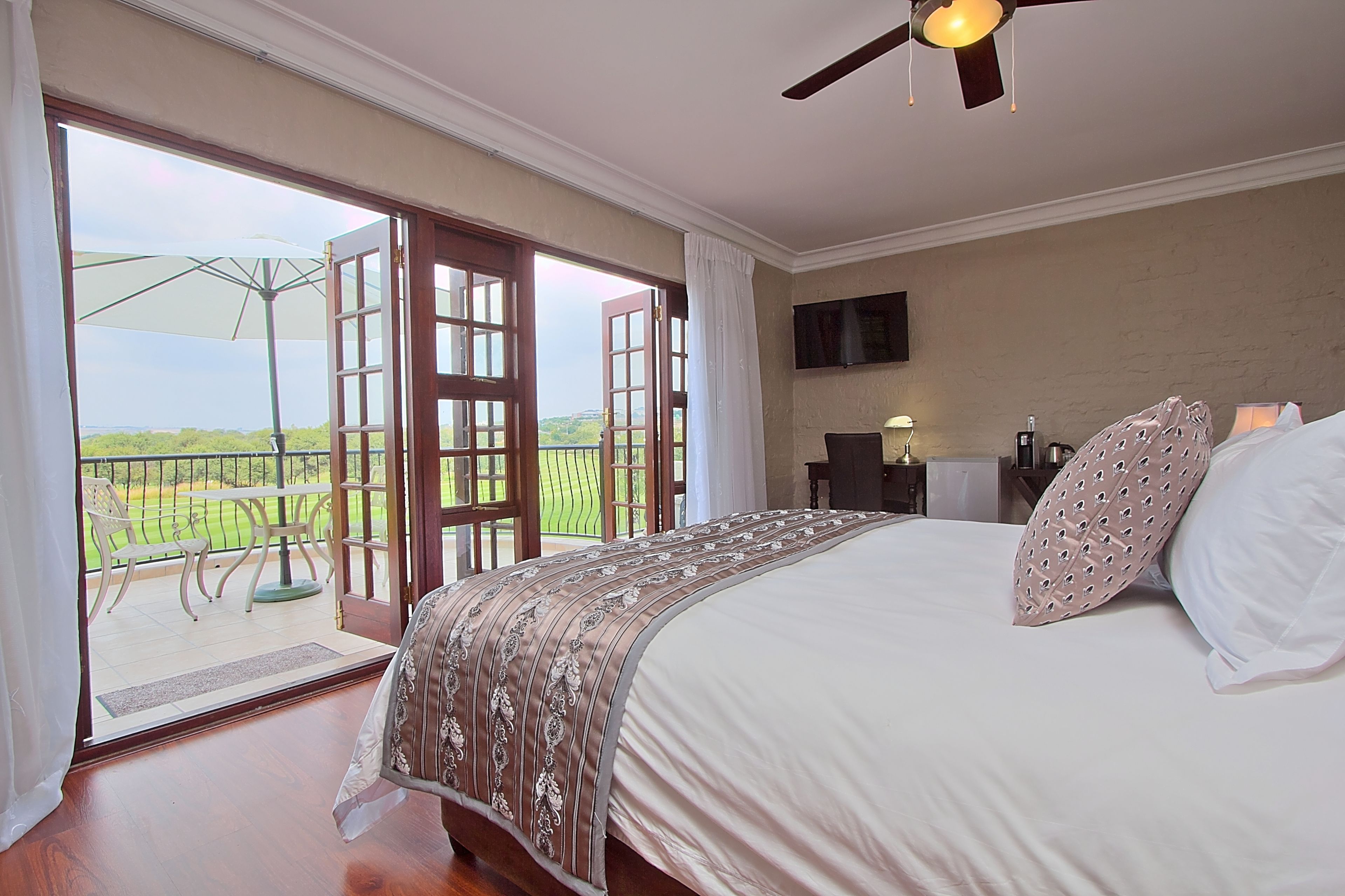 A bedroom with a large bed, a ceiling fan, a TV, and a balcony with an umbrella.