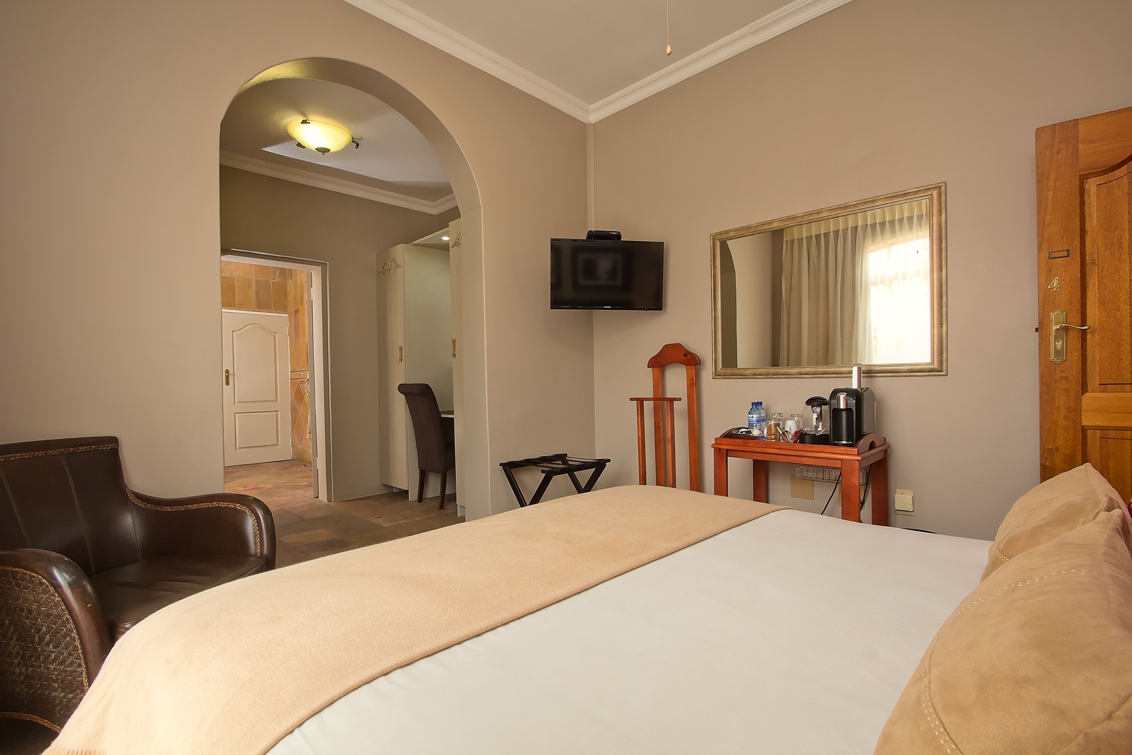 Une chambre d’hôtel avec un grand lit, un téléviseur fixé au mur, un bureau avec un miroir et une porte.
