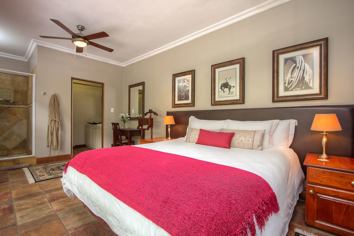 A hotel room with a large bed, two bedside lamps, a ceiling fan, and framed pictures on the wall.