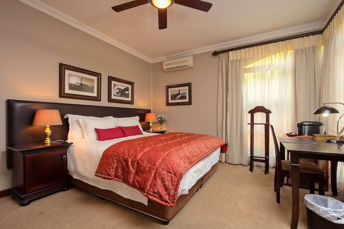 A hotel room with a large bed, a desk with a chair, a ceiling fan, and framed pictures on the wall.