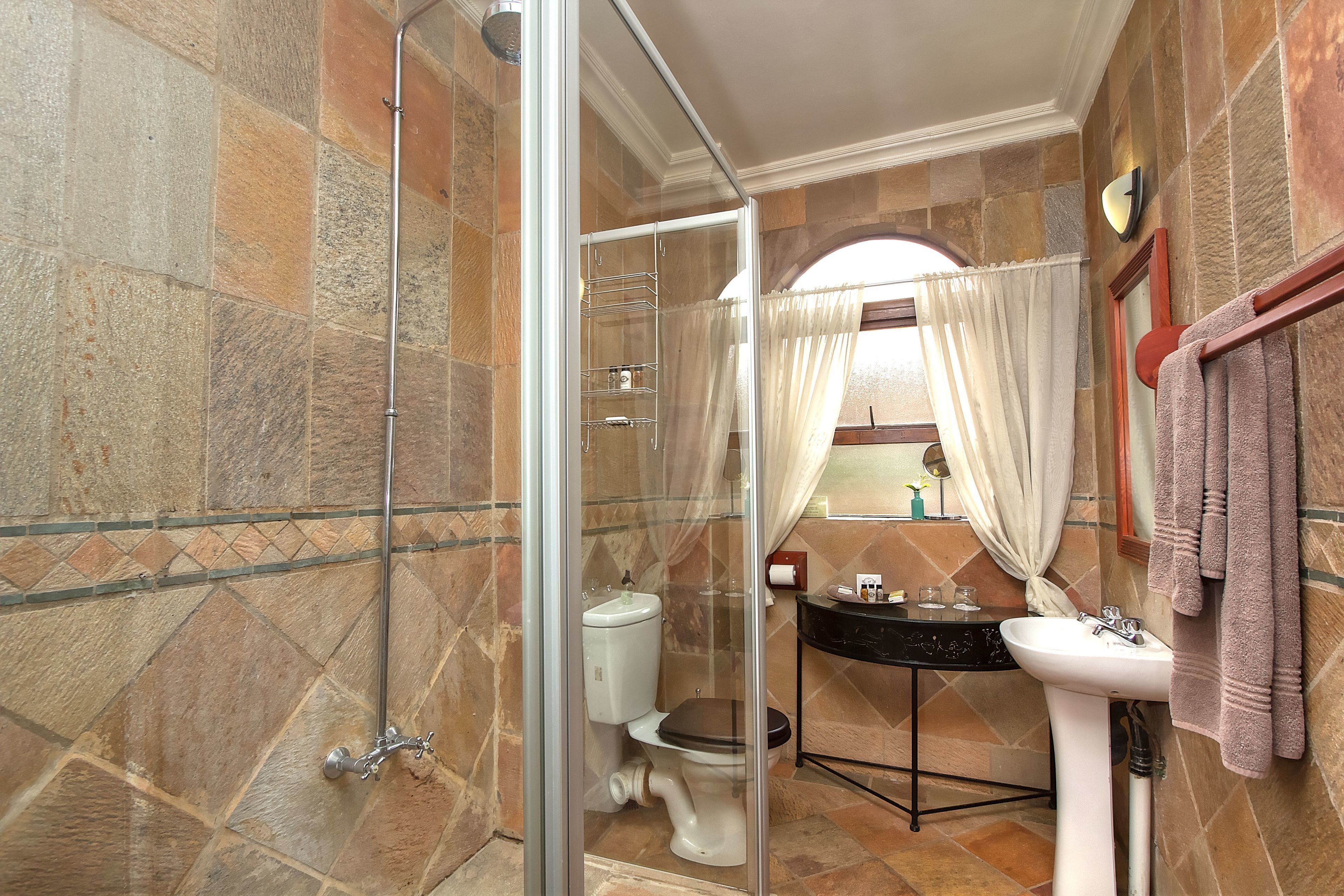 A bathroom with a glass-enclosed shower, a toilet, a sink, and a mirror.