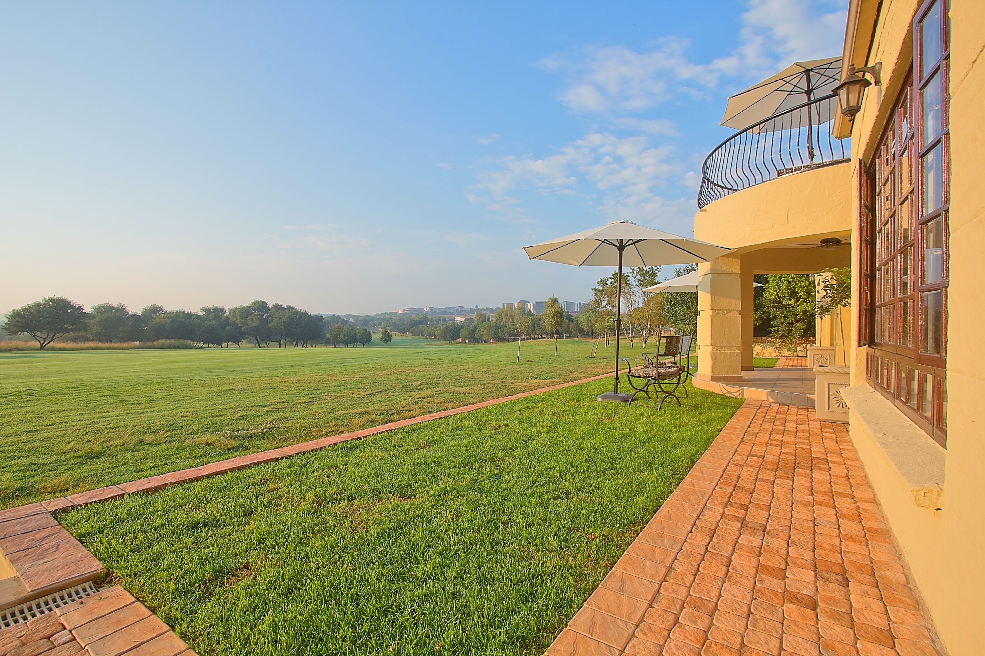A courtyard with a paved walkway, a grassy field, and a building with a balcony and outdoor seating area.