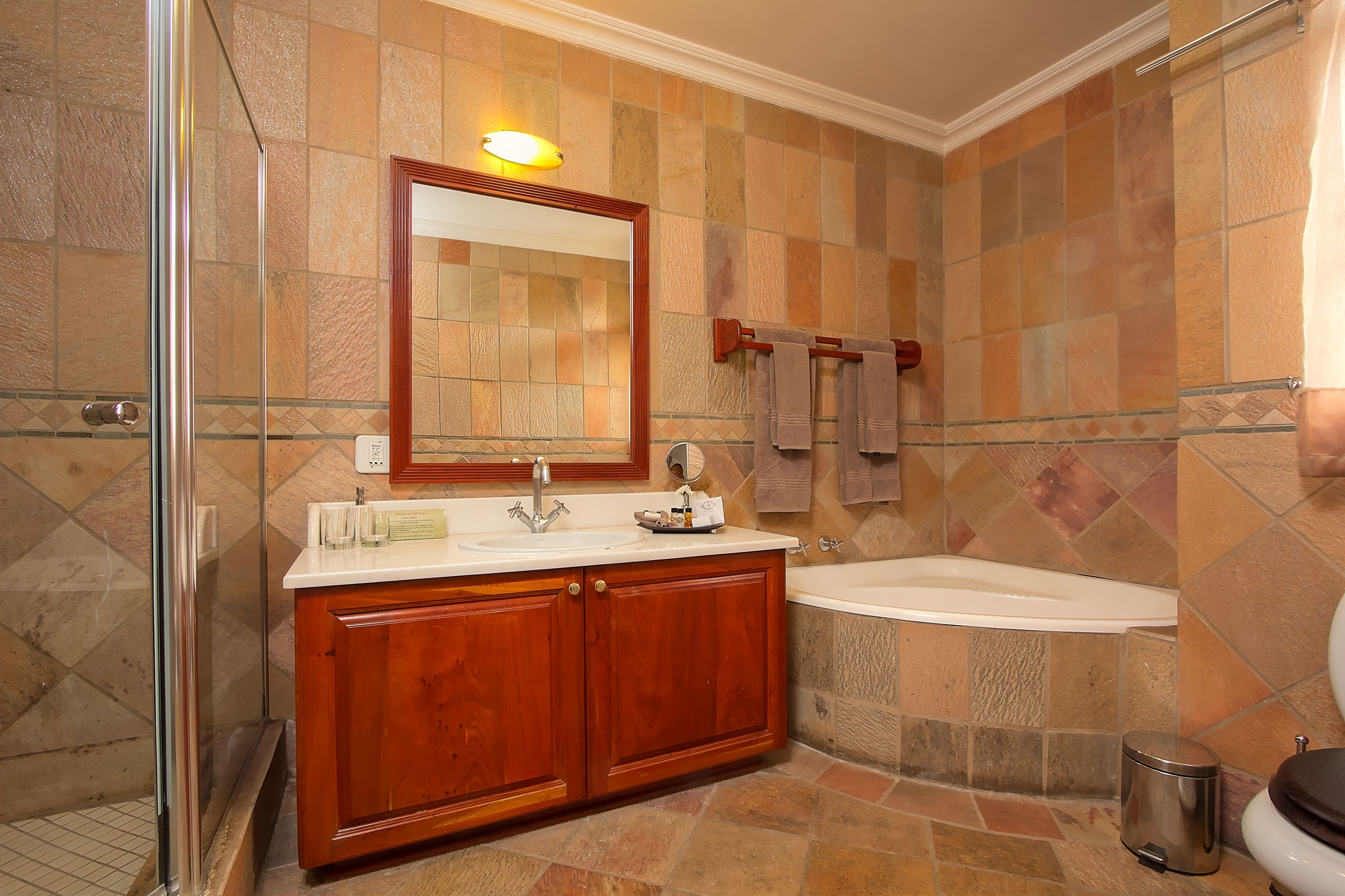 A bathroom with a glass shower enclosure, a wooden vanity with a sink, a bathtub, and a toilet.