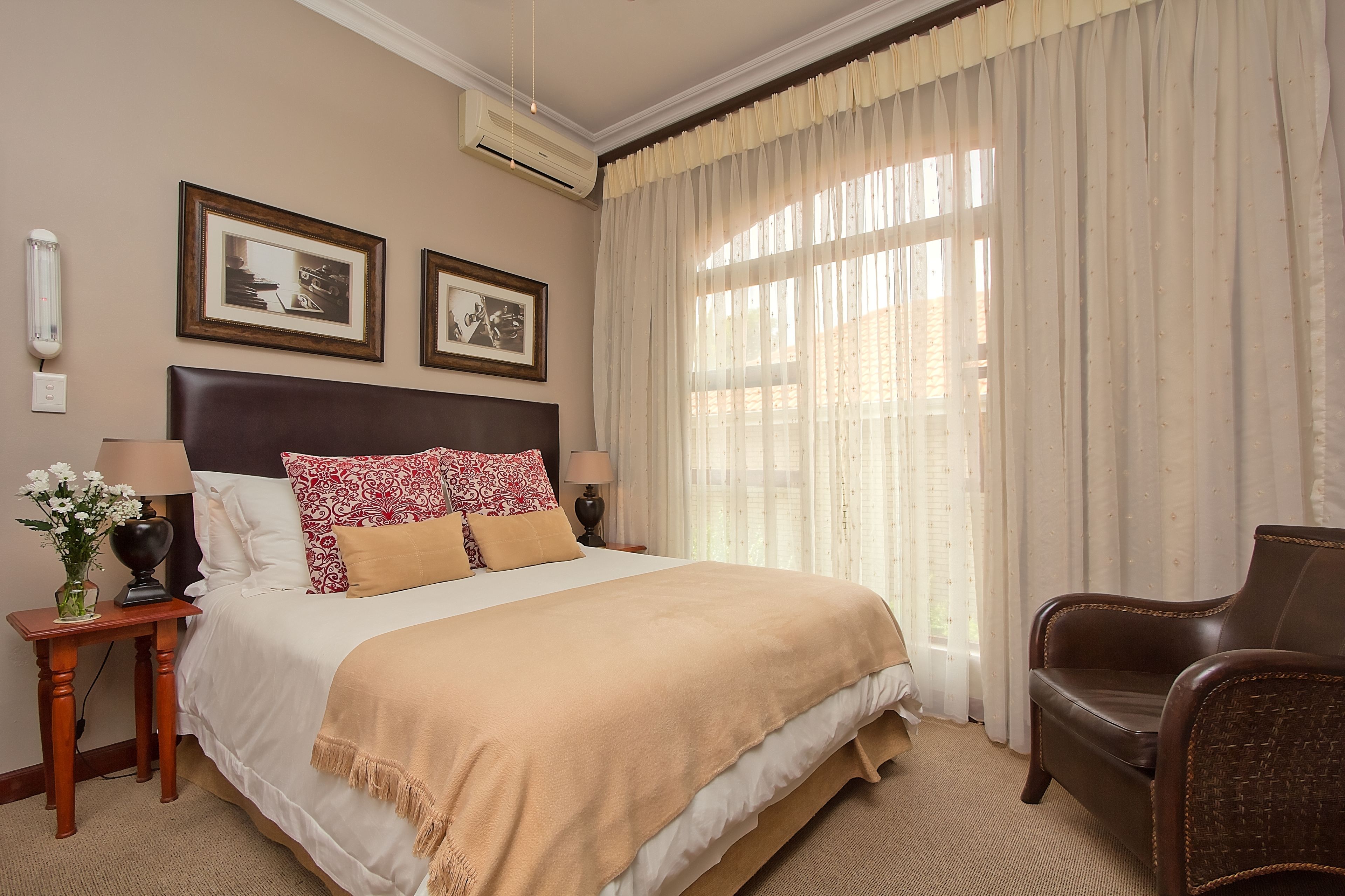 A neatly arranged hotel room with a large bed, a chair, a small table with a lamp, and two framed pictures on the wall.