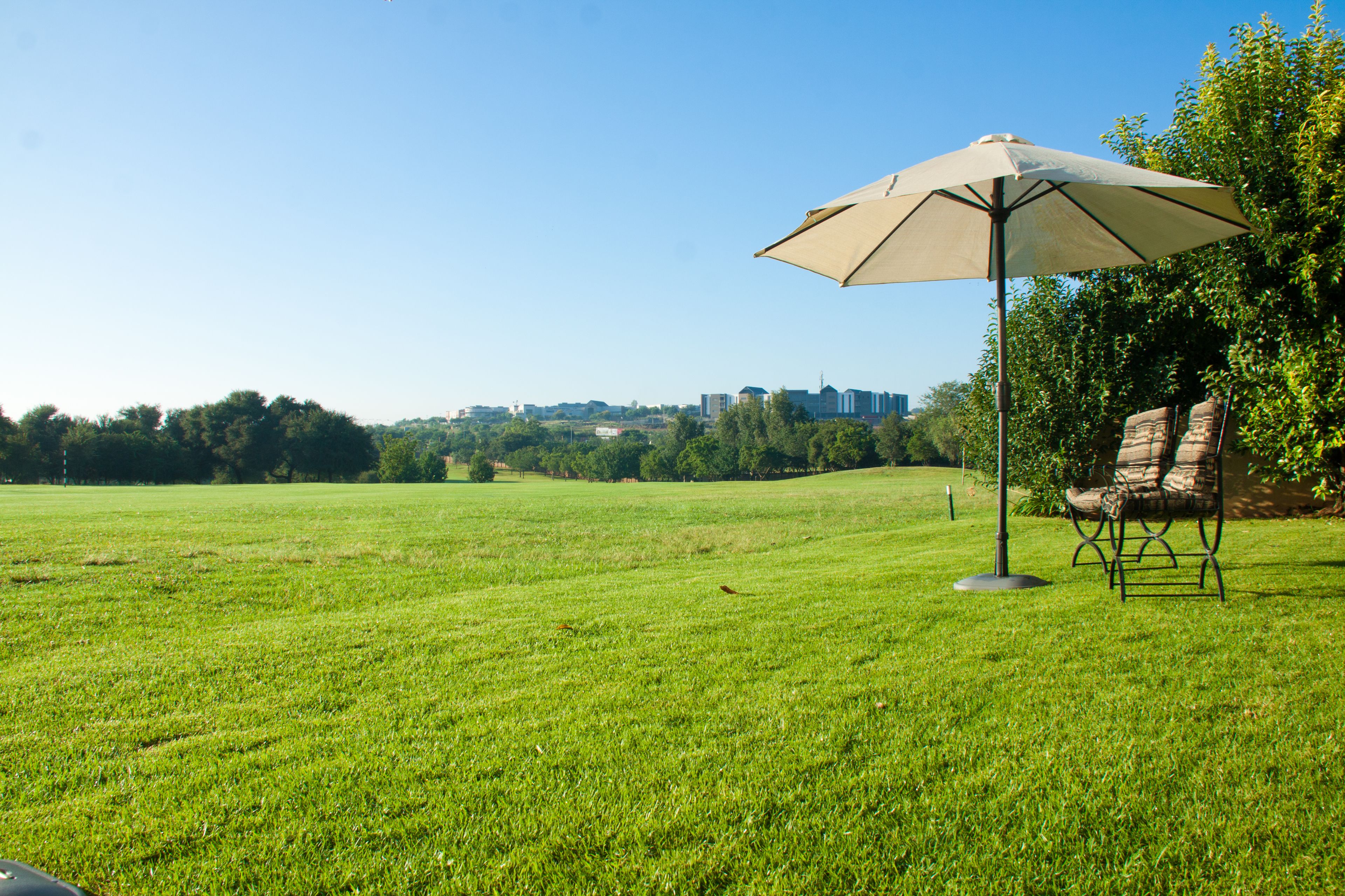 Un campo cubierto de césped con un área de estar al aire libre, que incluye una silla y una sombrilla.