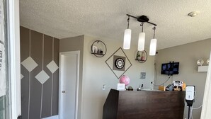 A modern living room with a dark wooden reception desk, a patterned rug, a wall clock, and a mounted television. - Travellers Inn Pembroke (Pembroke)