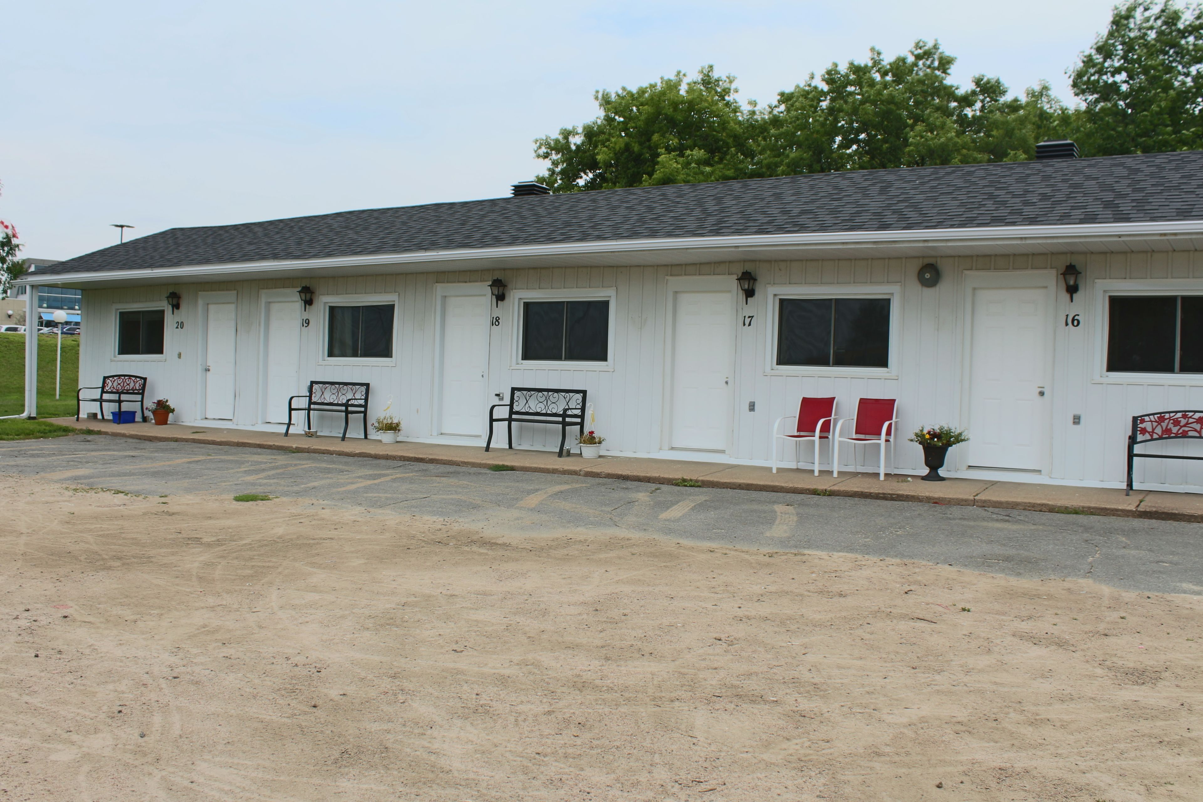 A motel with numbered doors, outdoor seating, and a parking lot.